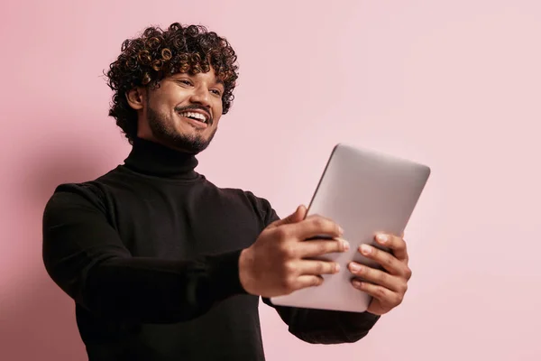 ハンサムなインド人男性保持デジタルタブレットとピンクの背景に笑顔 — ストック写真