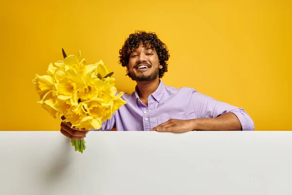ハンサムなインド人男性ストレッチアウト花花束に対して黄色の背景 — ストック写真
