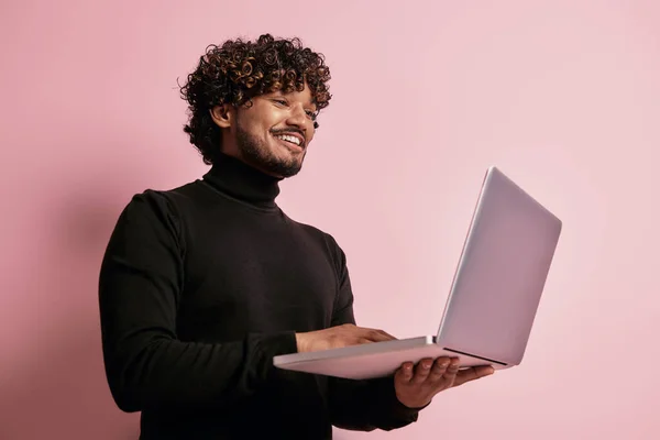 英俊的印度人 用笔记本电脑 在粉色背景下微笑 — 图库照片