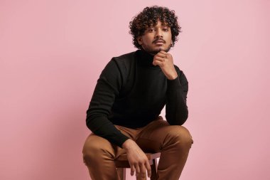 Yakışıklı Hintli adam pembe arka planda sandalyede oturuyor.