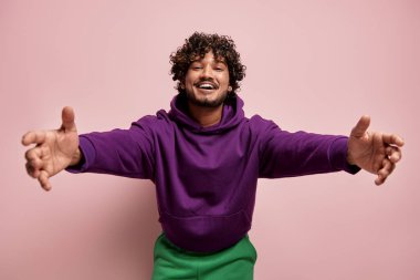Mutlu genç Hintli adam pembe arka plana sarılmak için ellerini uzatıyor.