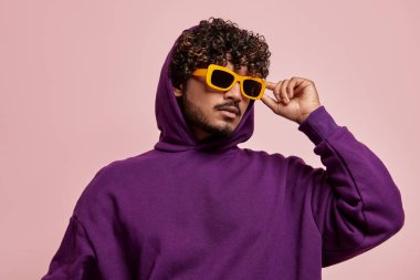 Yakışıklı genç Hintli adam pembe arka planda güneş gözlüğünü ayarlıyor.