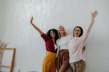 Duvara yaslanırken kollarını açık tutan üç mutlu olgun kadın.