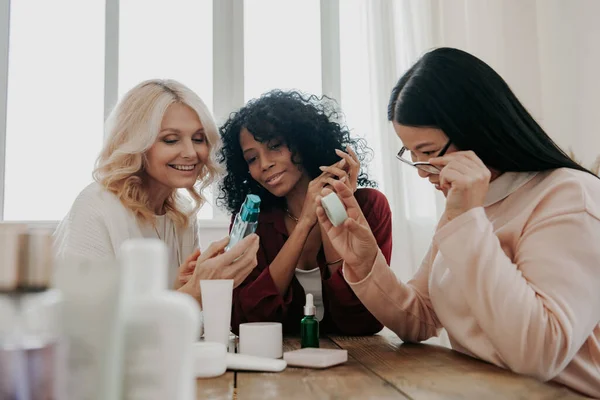Tři Dospělé Ženy Zkoumá Kosmetické Výrobky Zatímco Sedí Stolem Spolu — Stock fotografie