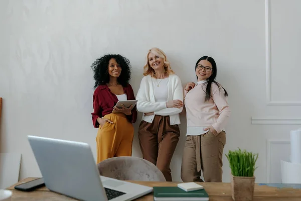 オフィスの壁にもたれながら笑顔の3人の現代的な成熟した女性 — ストック写真