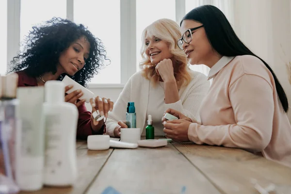 三个快乐的成熟女人一起坐在办公桌前测试美容产品 — 图库照片