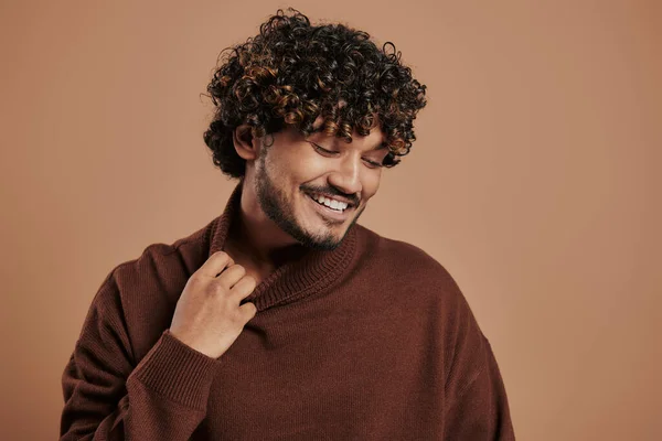 スタイリッシュなインド人男性ストレッチセーターカラーと笑顔で茶色の背景 — ストック写真