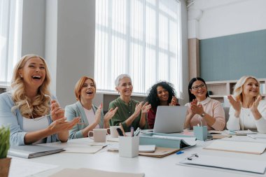 Bir grup mutlu iş kadını ofiste toplanırken alkışlıyorlar.
