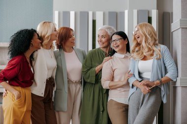 Bir grup mutlu olgun kadın ofiste yan yana durup gülümsüyor.