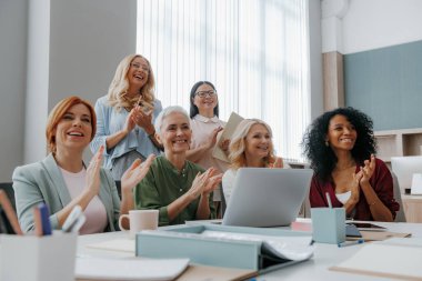 Bir grup olgun kadın ofiste işletme eğitimi alırken alkışlıyorlar.