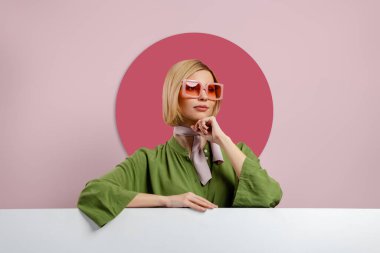 Moda gözlüklü, pembe arka planda fotokopi odasına yaslanmış şık genç bir kadın.