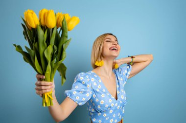 Çekici genç bir kadın mavi arka planda sarı laleler tutuyor.