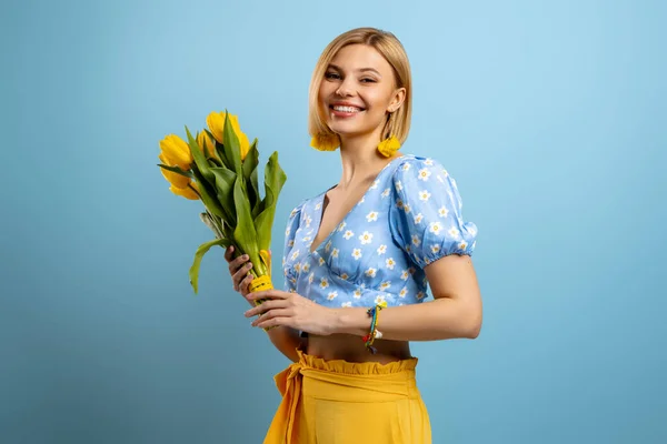 stock image Happy young woman holding bunch of tulips and smiling against blue background