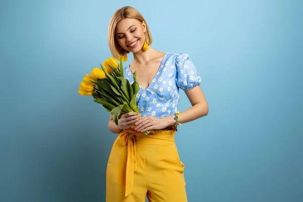 Stock image Joyful young woman holding bunch of tulips and smiling against blue background