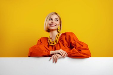 Güzel genç bir kadın fotokopi odasına yaslanıyor ve sarı arka plana gülümsüyor.