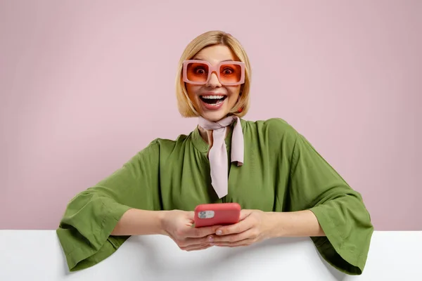 Модна Молода Жінка Тримає Смартфон Виглядає Збуджено Рожевому Фоні — стокове фото