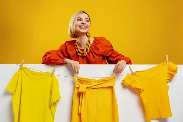 迷人的年轻女子在黄色背景的衣服上挂着五颜六色的衣服 — 图库照片