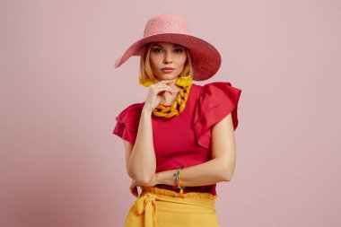 Zarif şapkalı çekici bir genç kadın pembe arka planda el ele tutuşuyor.