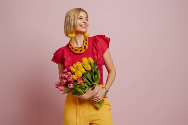 Bir sürü lale tutan ve pembe arka planda gülümseyen çekici genç bir kadın.