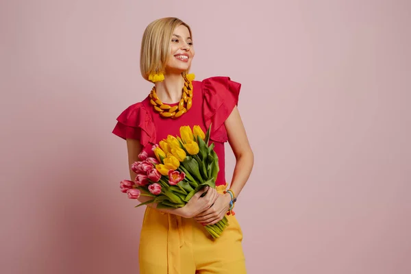 stock image Attractive young woman holding bunch of tulips and smiling against pink background