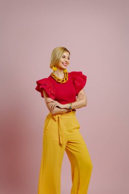 Renkli arka planda dikilen şık giyinmiş, gülümseyen zarif bir genç kadın.