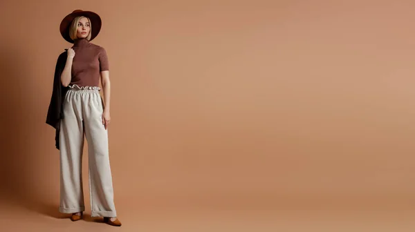 stock image Full length of fashionable young woman in elegant hat standing against brown background