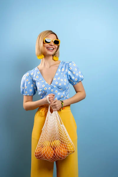 Beautiful Young Woman Carrying Mesh Bag Fresh Oranges Blue Background — Stock Photo, Image