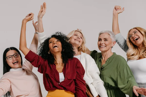 Multi-ethnic group of happy mature women gesturing and smiling against grey background