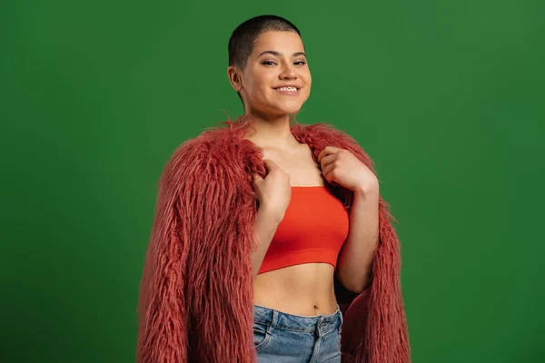 Beautiful short hair woman in fluffy jacket smiling while standing against green background