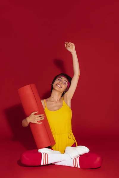 ハッピーフィット女性でレトロスポーツウェア保持運動マットとジェスチャーに対して赤背景 — ストック写真