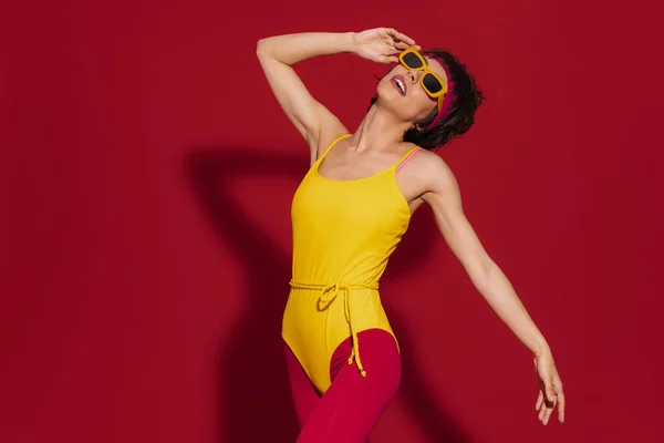 Mulher Bonita Retro Estilo Sportswear Ajustando Óculos Contra Fundo Vermelho — Fotografia de Stock