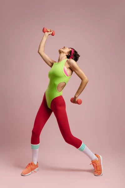 幸せなフィット女性でレトロなスタイルのスポーツ服を練習ダンベルで色の背景 — ストック写真