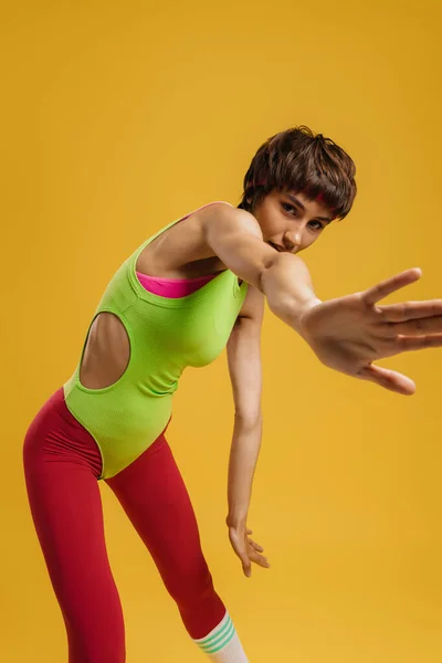 若いですフィット女性でレトロスタイルのスポーツ服ストレッチ手に対して黄色の背景 — ストック写真