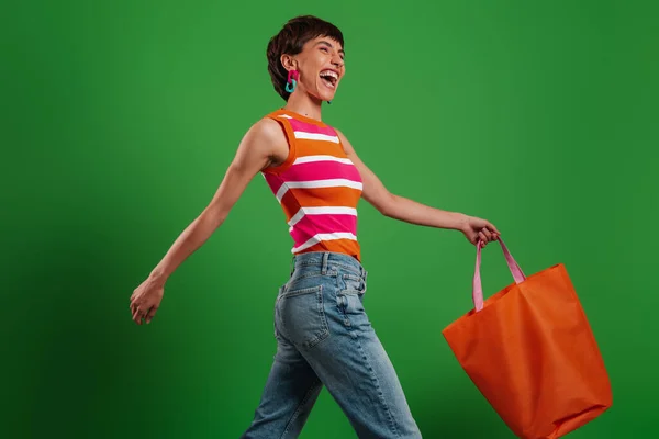 Jovem Feliz Carregando Saco Compras Enquanto Caminha Contra Fundo Verde — Fotografia de Stock