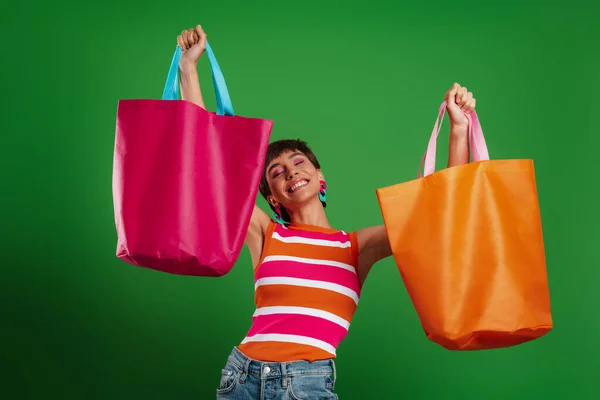 Счастливая Молодая Женщина Показывает Свои Красочные Сумки Покупок Стоя Зеленом — стоковое фото