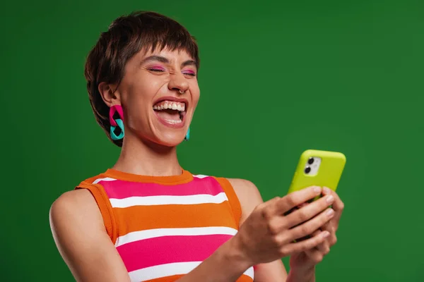 Захоплена Молода Жінка Тримає Смартфон Посміхається Стоячи Зеленому Тлі — стокове фото