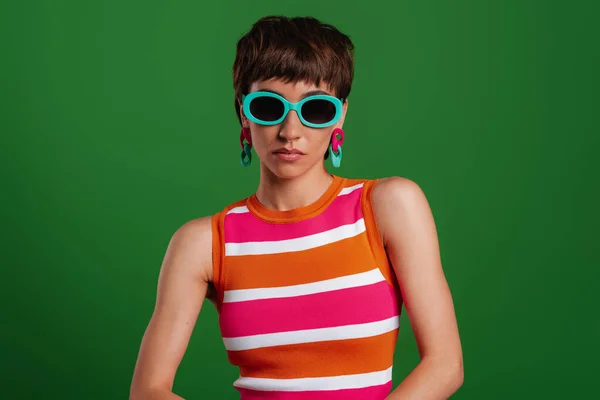 緑を背景に立ちながらカメラを見ながら流行のメガネでスタイリッシュな若い女性 — ストック写真