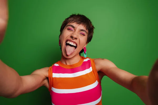 Zabawna Młoda Kobieta Robi Selfie Wystający Język Stojąc Zielonym Tle — Zdjęcie stockowe
