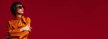 Gözlüklü, kırmızı arka planda duran zarif kısa saçlı kadının portresi.