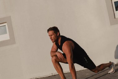 Kendine güvenen genç erkek sporcu şehir binasına karşı sabah egzersizi yapıyor.