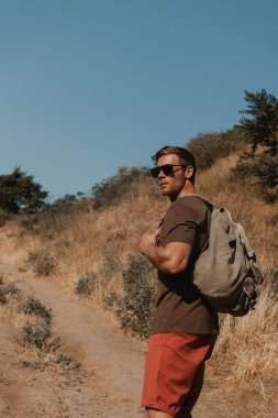 Sırt çantalı kendine güvenen erkek maceracı dağ yolunda yürüyor.