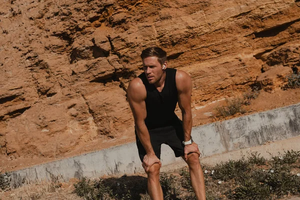 身穿运动服的疲惫的年轻运动员站在岩石山外 — 图库照片
