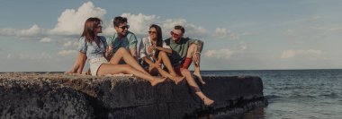 Birlikte deniz kenarında kaygısızca vakit geçirirken biranın keyfini çıkaran bir grup mutlu genç arkadaş.