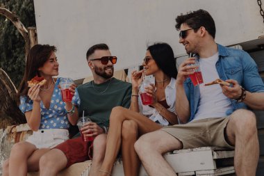 Bir grup neşeli arkadaş birlikte dışarıda vakit geçirirken yemek ve içeceklerin tadını çıkarıyorlar.