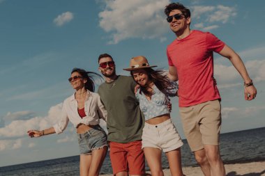 Bir grup mutlu genç arkadaş sahilde birlikte vakit geçirirken birbirlerine bağlanıyorlar ve gülümsüyorlar.