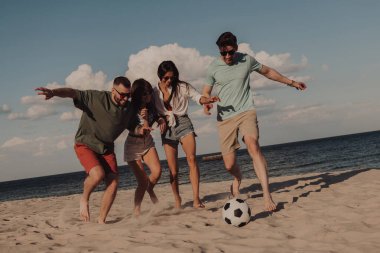 Bir grup genç futbol oynuyor ve sahilde birlikte eğleniyor.