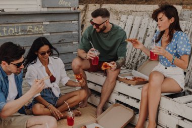 Mutlu genç arkadaşlar pizzayı ve içkiyi birlikte içiyorlar.