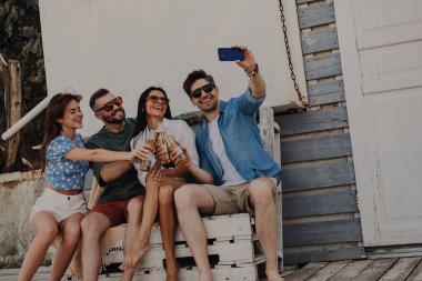 Bir grup mutlu arkadaş dışarıda bira içerken akıllı telefondan selfie çekiyorlar.