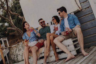 Bir grup mutlu arkadaş birlikte dışarıda vakit geçirirken yemek ve içeceklerin tadını çıkarıyorlar.