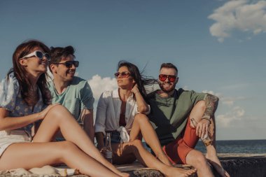 Birlikte deniz kenarında vakit geçirirken konuşan ve gülümseyen bir grup genç arkadaş.